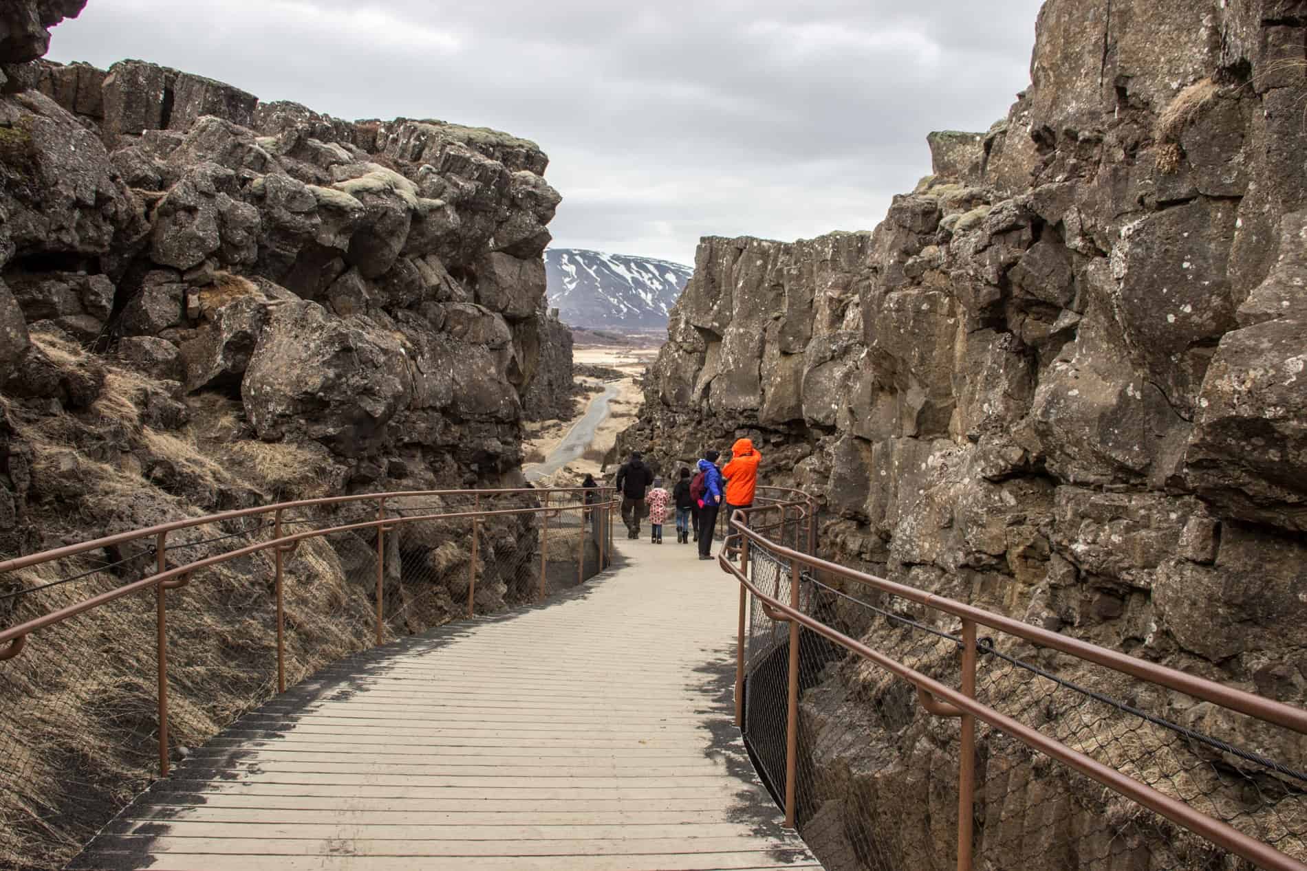 A group of people walking on a wooden platform through the rocky split of tectonic plates in Pingvellie National Park, Iceland. 