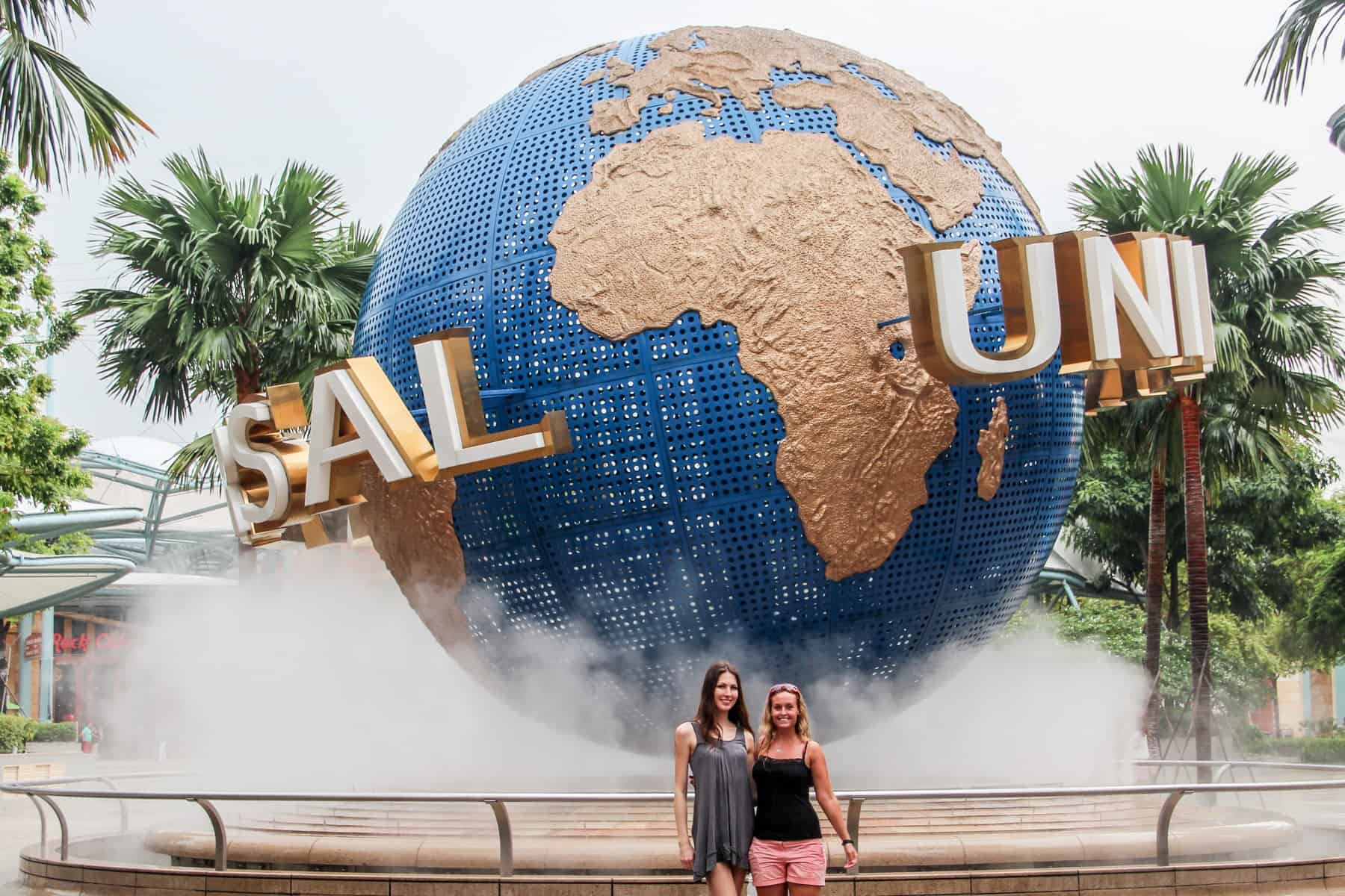 Two women stand outside the giant blue and gold globe logo of Universal Studios in Singapore