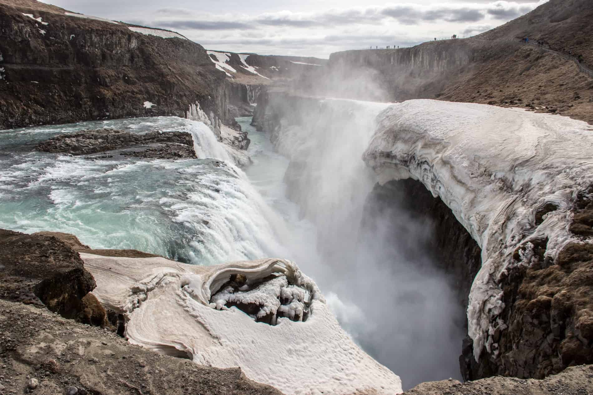 Cascading water falls between rock walls at the Gullfoss waterfall in Iceland.