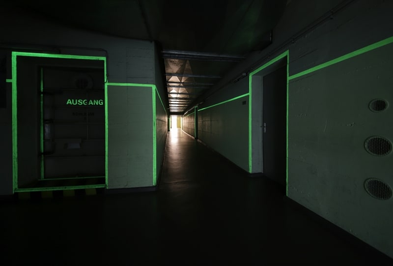 A blackened basement floor with doorways and corridors marked by neon green lights - part of a Berlin underground exhibition. 