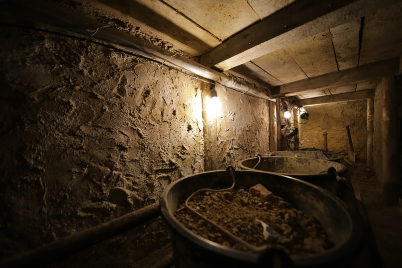 The inside of a dug out escape tunnels underground in Berlin, with three huge buckets filled with debris. 