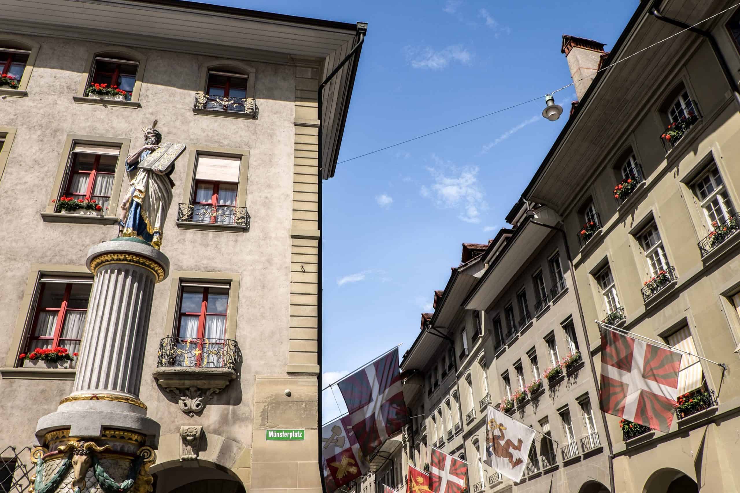 A religious figure in a blue robe on top of a columned water fountain on a main street in Bern Switzerland