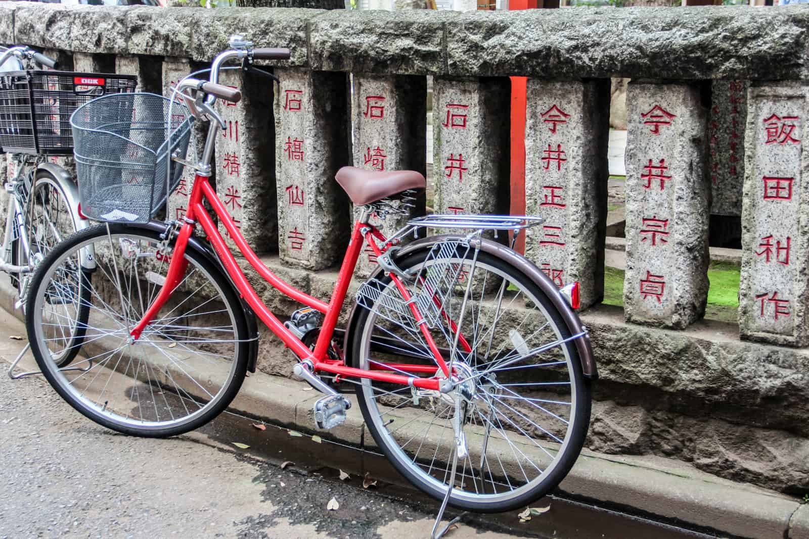 A red bike in front of a stone wall inscribed with red Japanese text. 