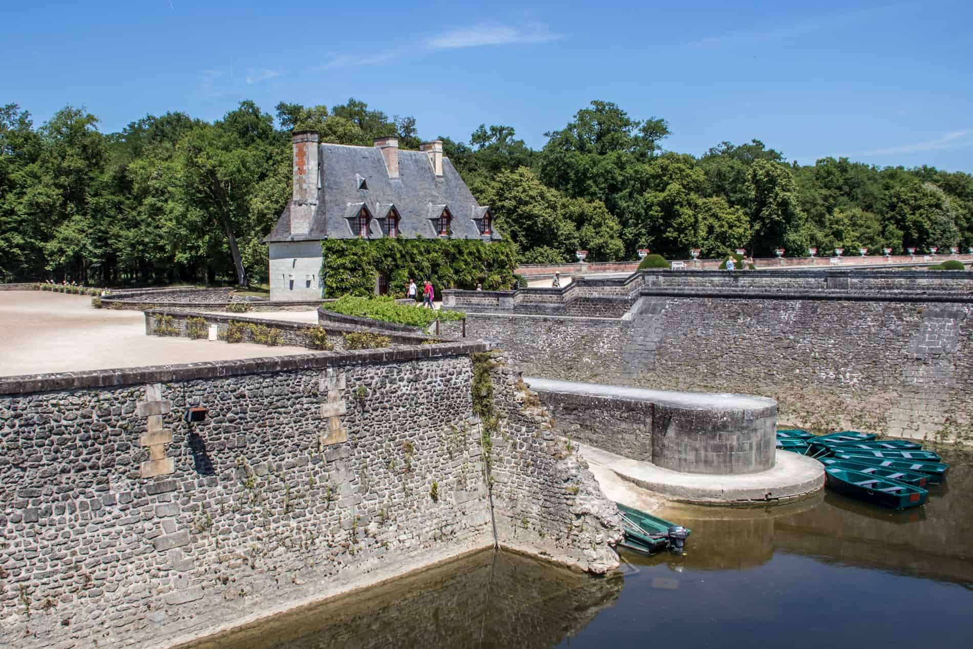 Green boats in the water below the old walls of Château de Chenonceau, Loire Valley. 