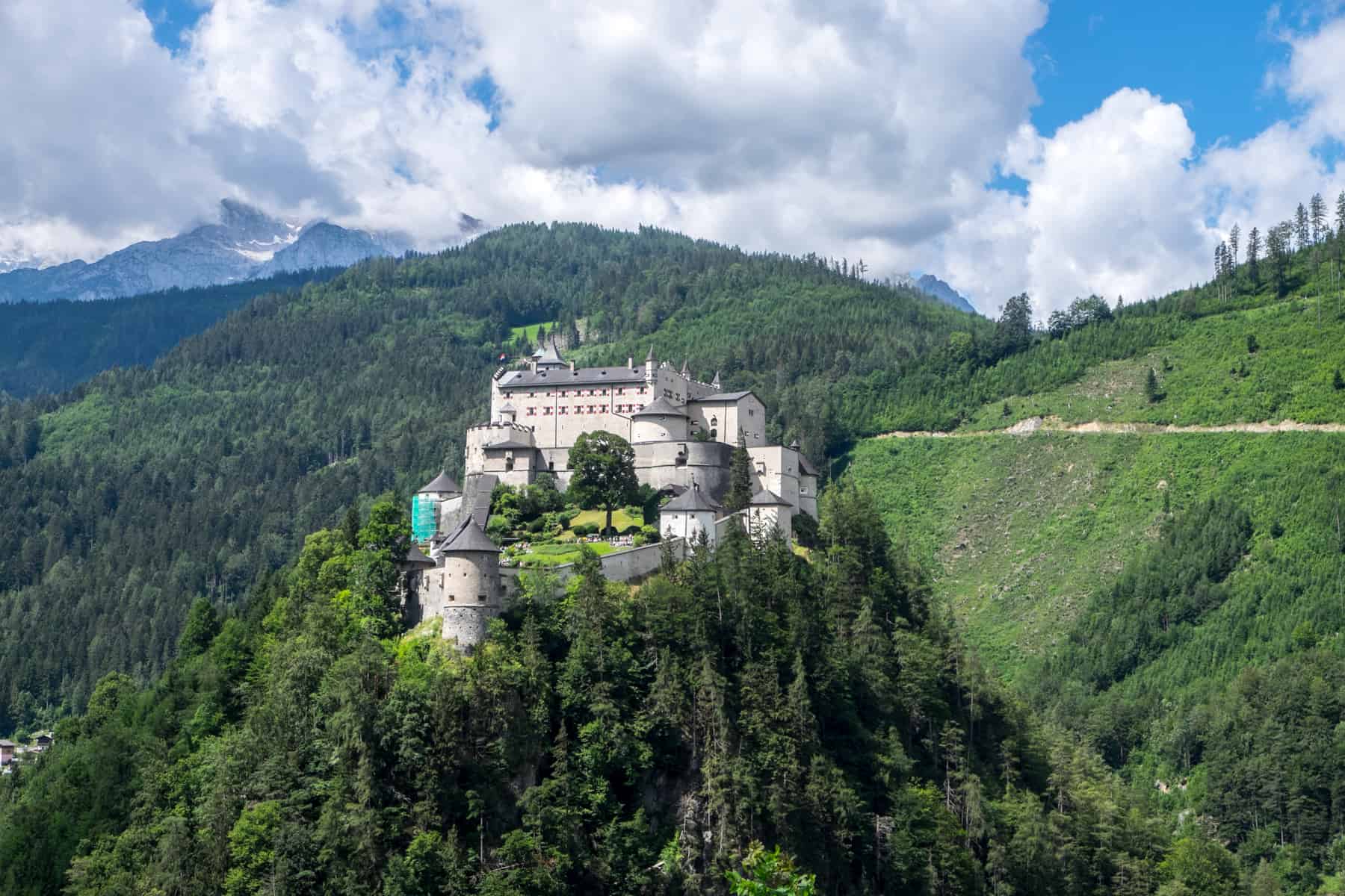 The elevated cream-coloured Burg Hohenwerfen fortress in Austria, perched on a small hill surrounded by a mound of thick trees