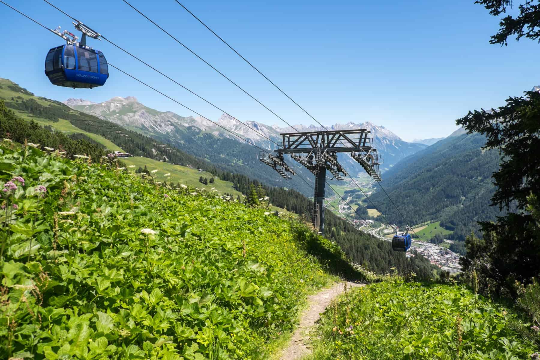 A royal blue cable cars glides over the green forested Galzig mountain in St Anton in summer