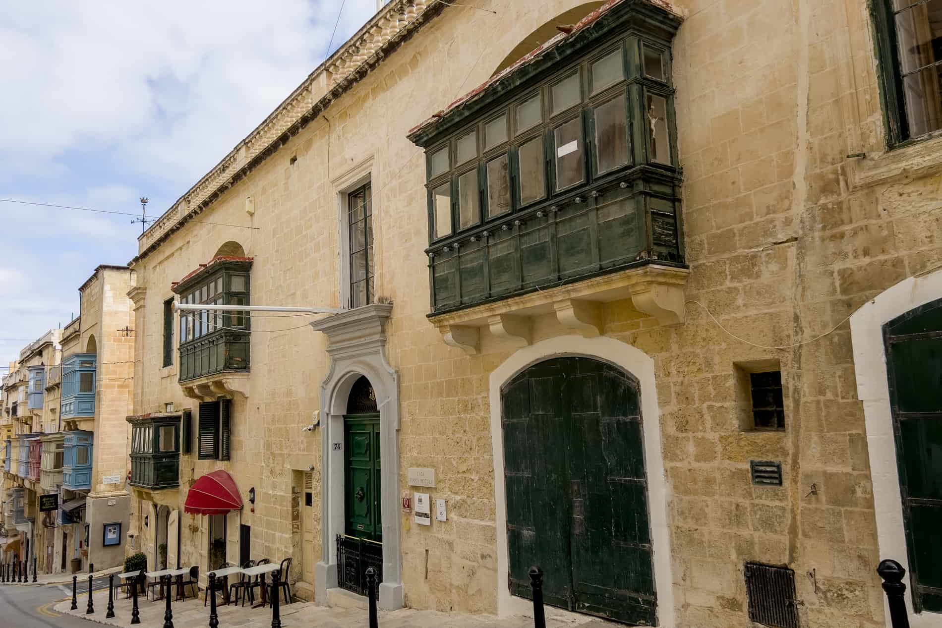 The rectangular golden stone noble house of Casa Rocca Piccola in Valletta, with dark green balconies and door shutters. 