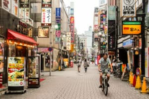 A man cycles down a street in Japan with neon lights and advertising.