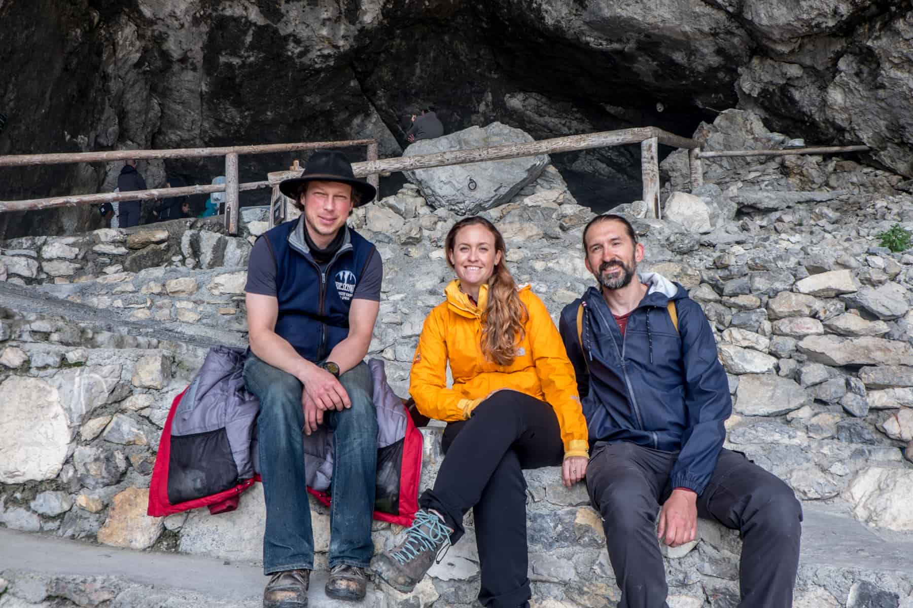 A guide from the Eisriesenwelt cave sits with a woman in orange and a man in blue outside the rocky entrance to the Eisriesenwelt ice cave in Austria