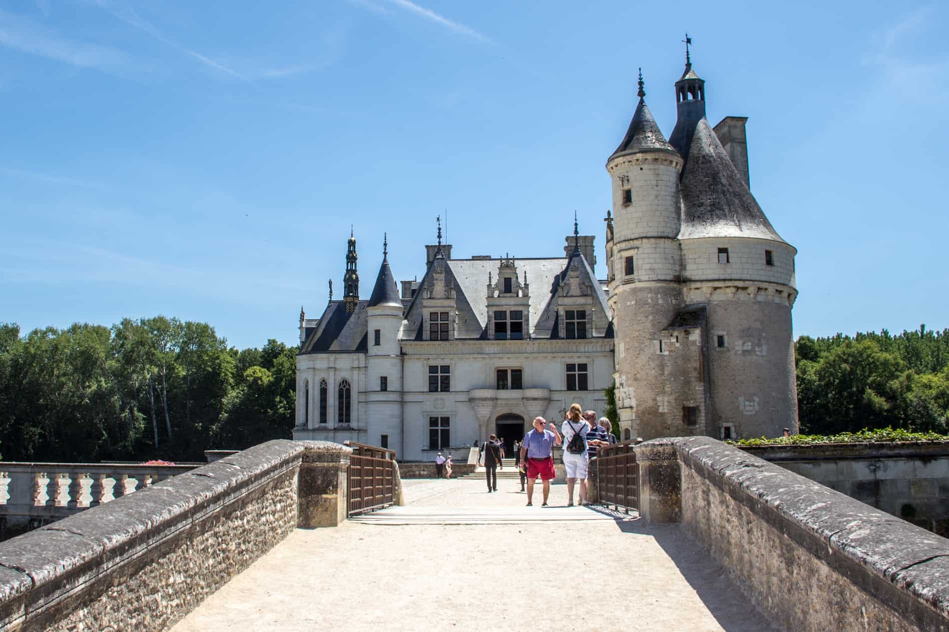 People walk over a wide stone bridge towards the entrance of the refined Château de Chenonceau in the Loire Valley, France. 