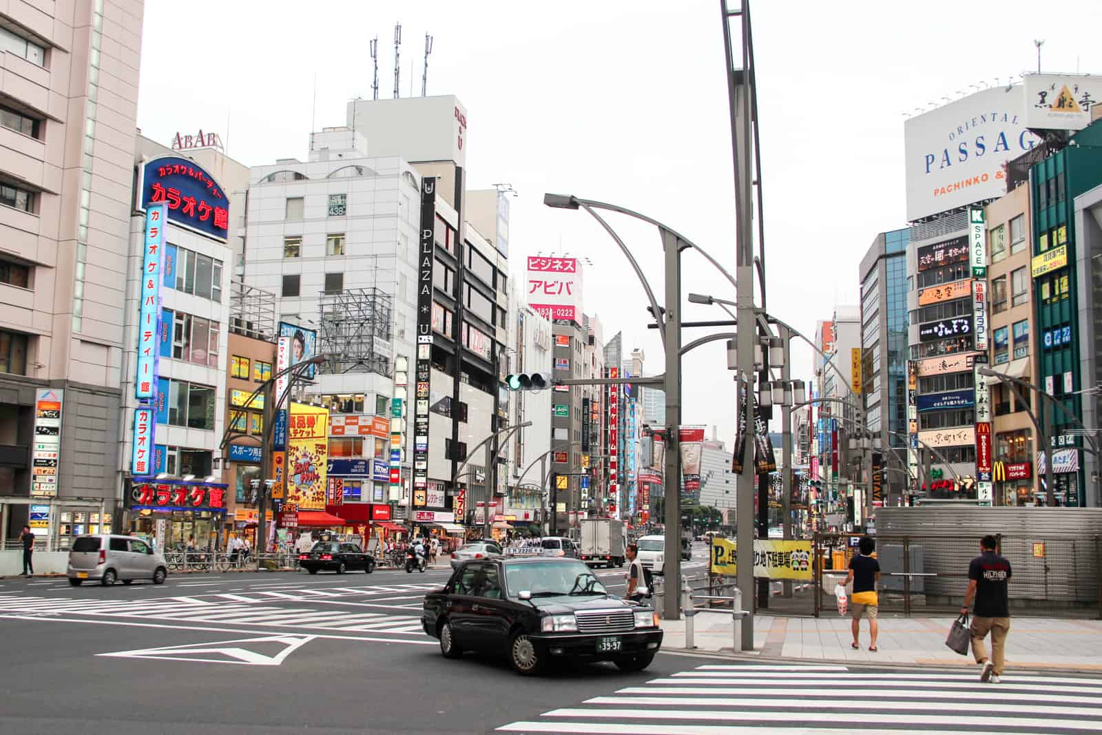 A black Japan taxi on Tokyo city roads lined with tall buildings covered in lights and advertising signs. 