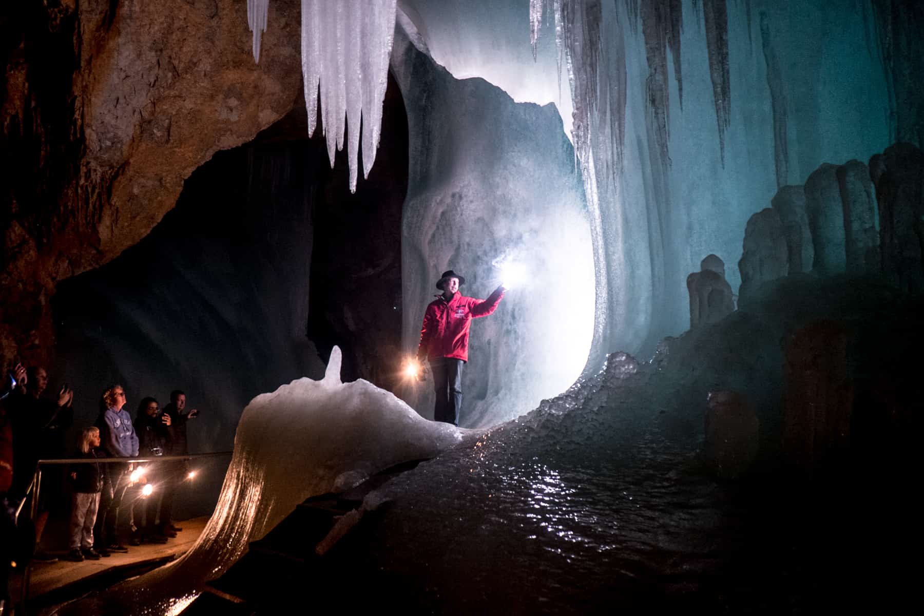 A guide in a red jacket stands in a circle of illuminated ice in the Eisriesenwelt cave. He's holding sparklers. A group looks on in wonder.
