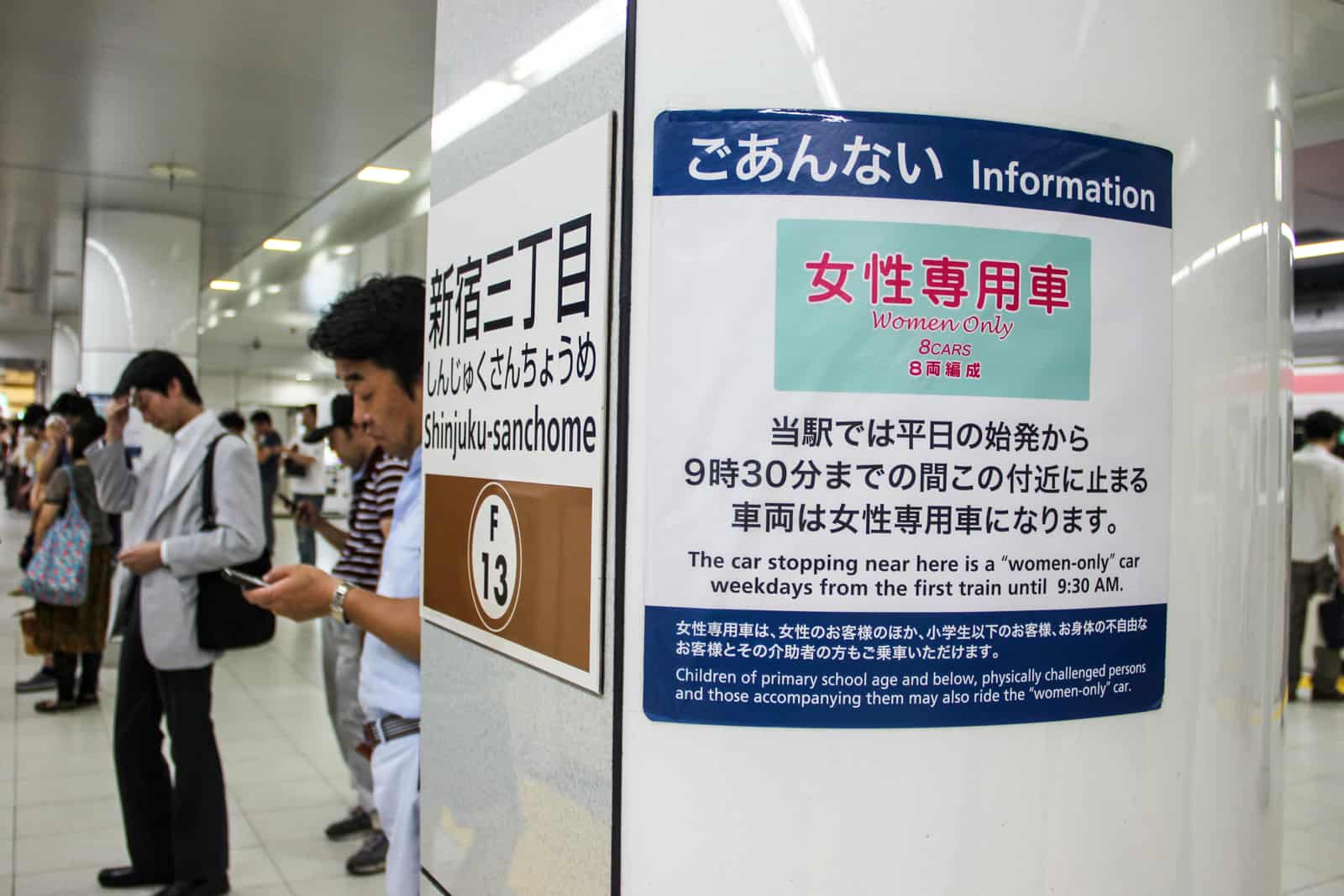 People waiting on Tokyo metro platform next to a sign indicating a women only carriage. 