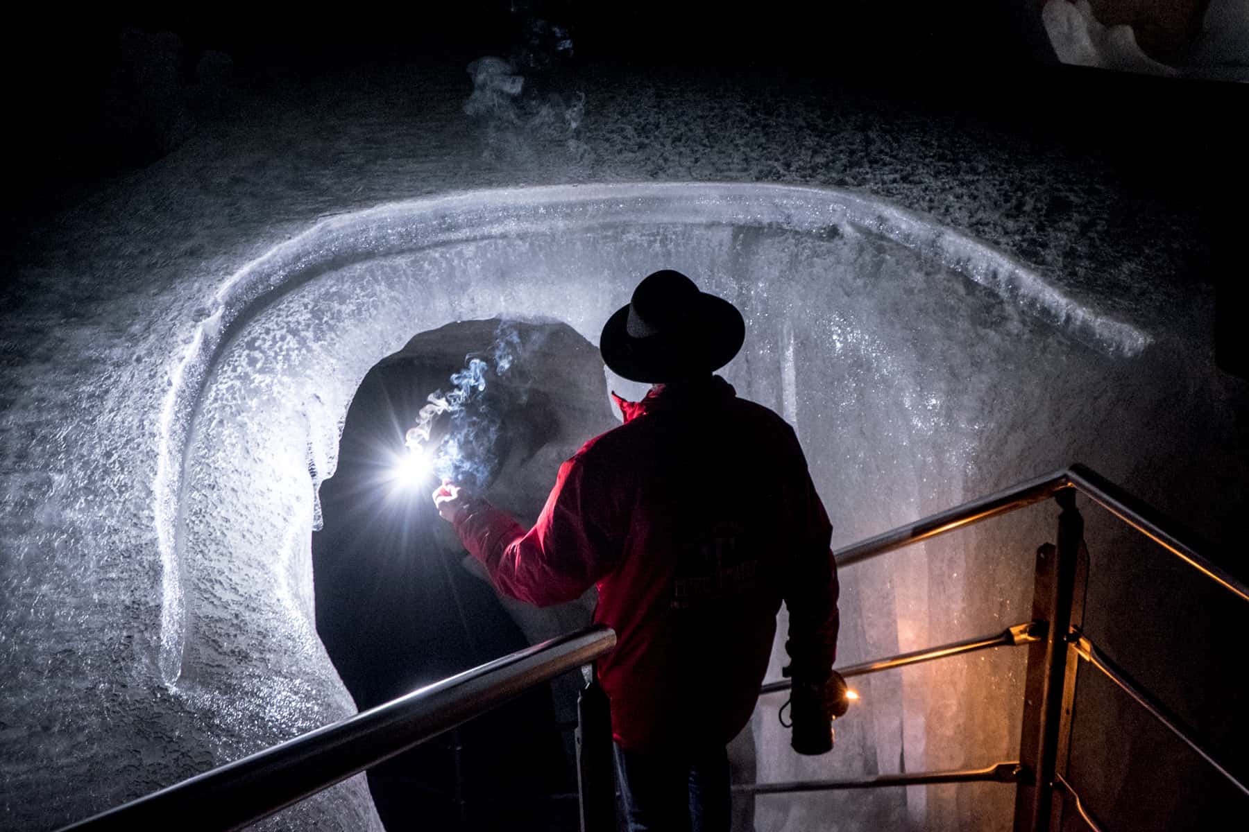 A man in a red jacket and black hat hots a light sparkler as he beings his entry into a tunnel of ice at Eisriesenwelt, Austria