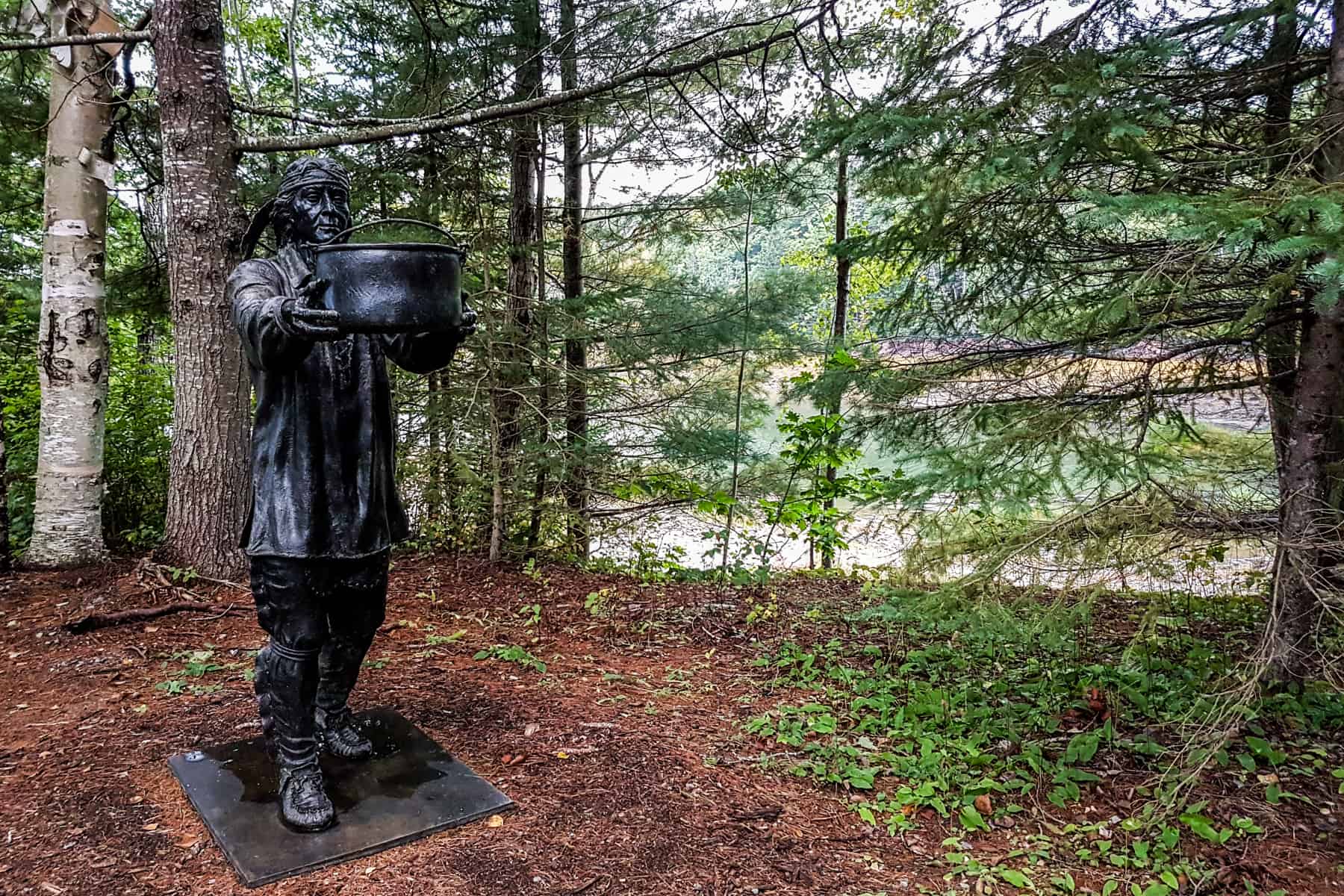 A black bronze statues holding a large bowl and depicting life on the settlement, standing within the Saint Croix Historical Site in Maine, US.