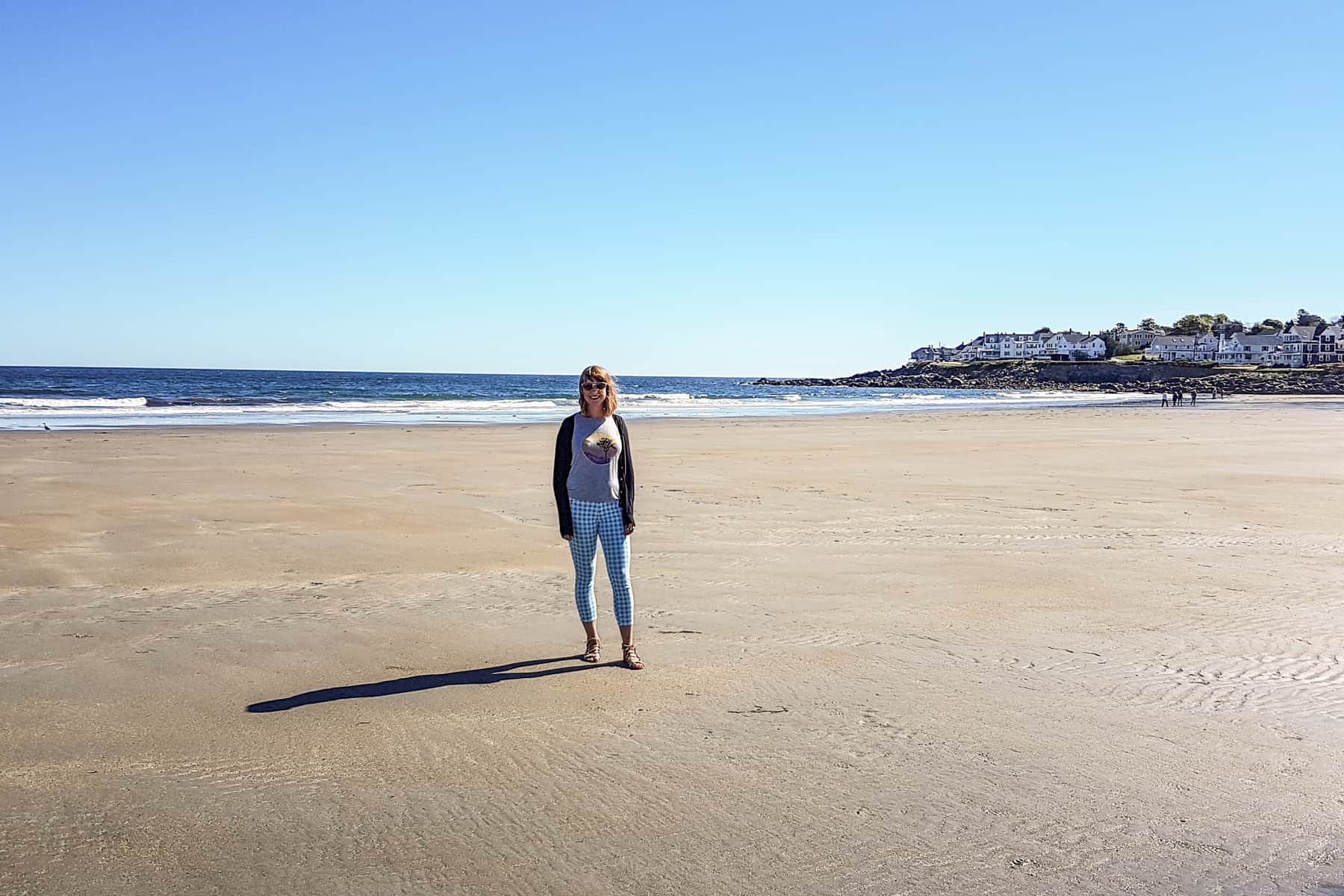 A woman stands on a wide yellow sand beach in York, Maine on the US Route 1 road. 