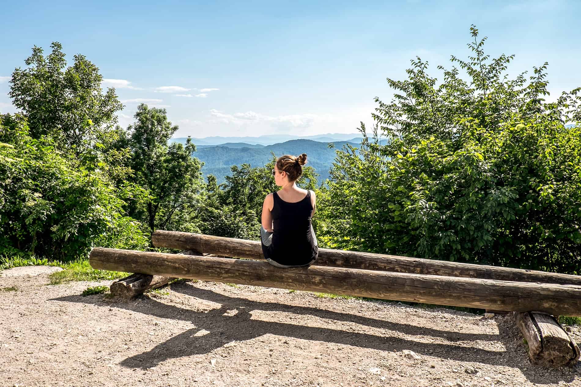 A woman sitting on a wooden log bench at the top of Smarna Gora Mountain in Slovenia.