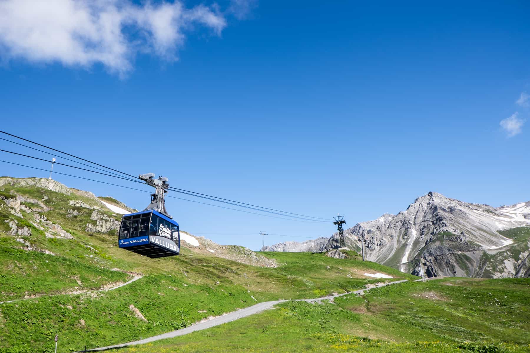 A blue cable car in St. Anton am Arlberg in summer glides up a green mountain peak