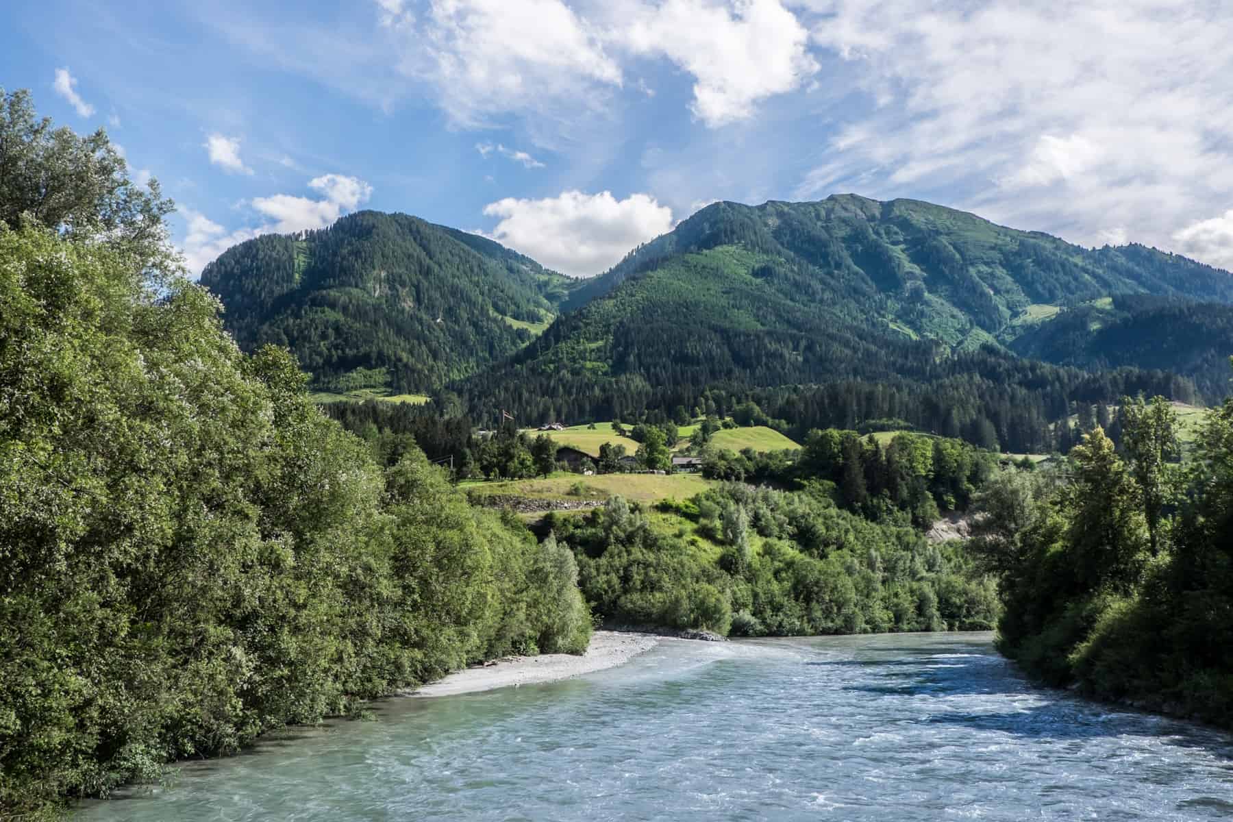 Crystal clear blue water flows towards a green meadow backed by grass coloured mountains in St. Johann im Pongau, Austria