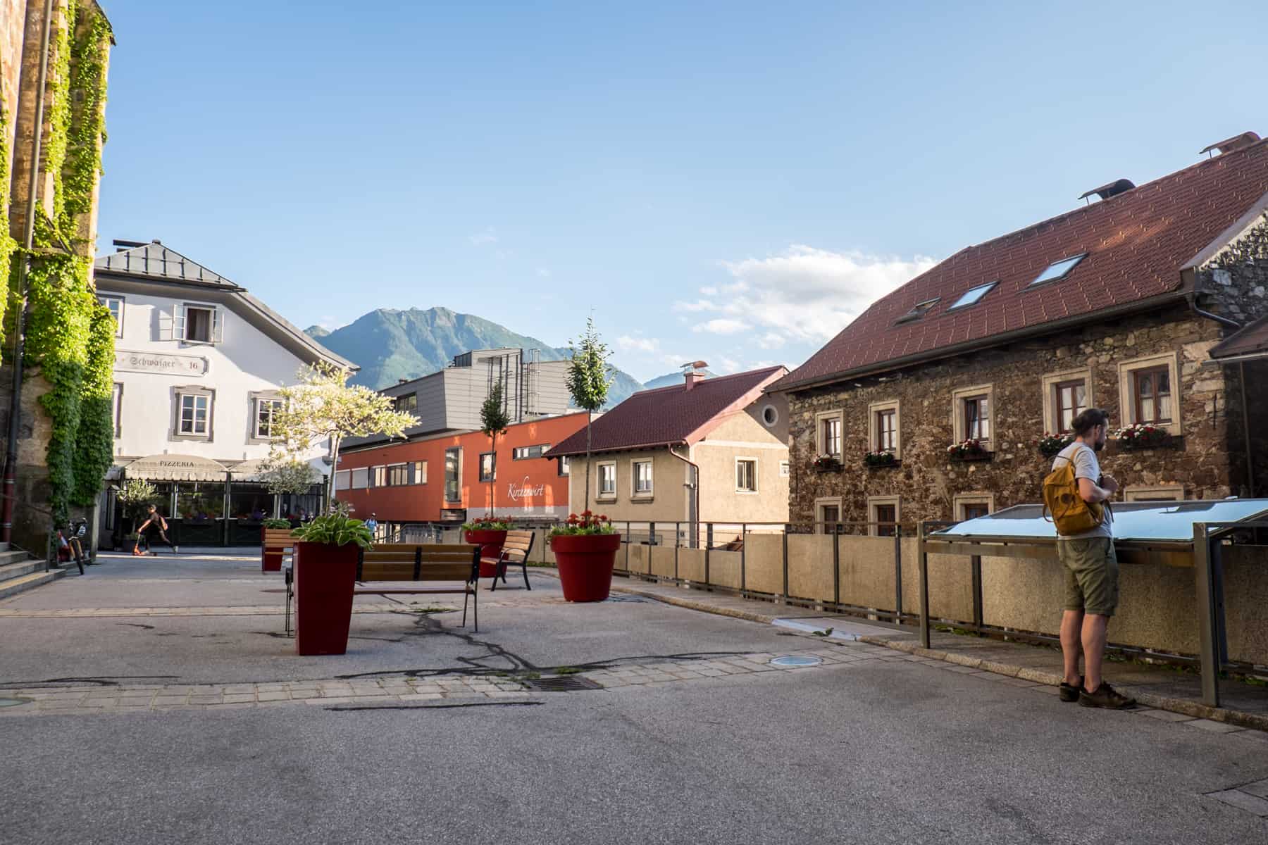 A man read from an information sign that sits at the end of a row of white, orange, beige and old brick houses in the city of St. Johann im Pongau