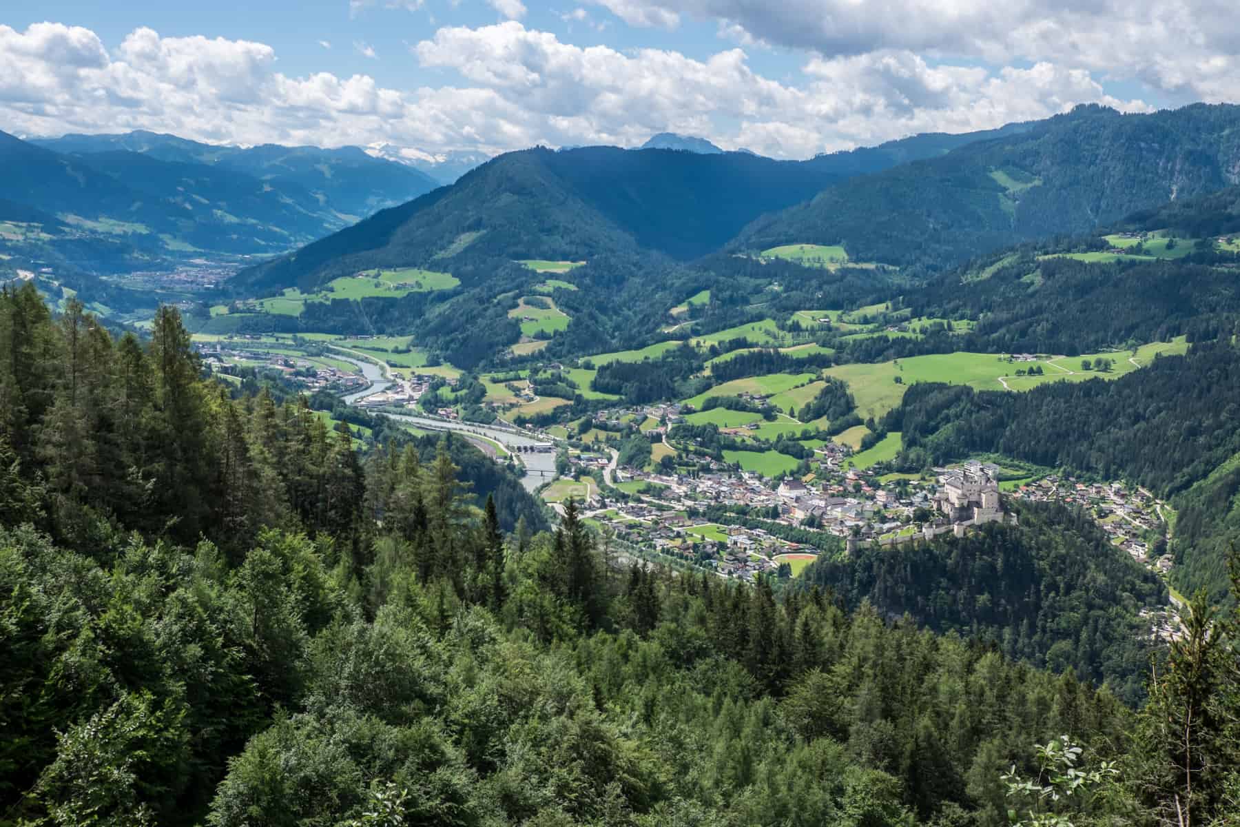 An elevated view of the Salzach River and surrounding valleys and cities, with forest on one side and the Austrian Alps on the other