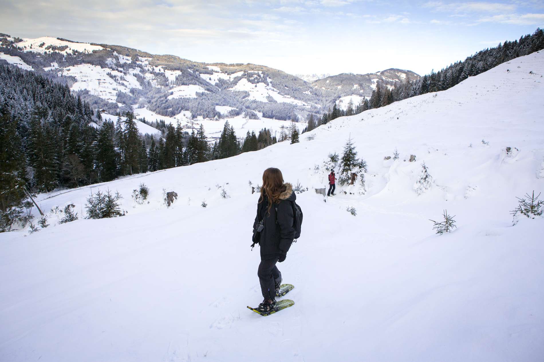 A woman in snowshoes looks out over a snow slope towards the Alps in Austria. 