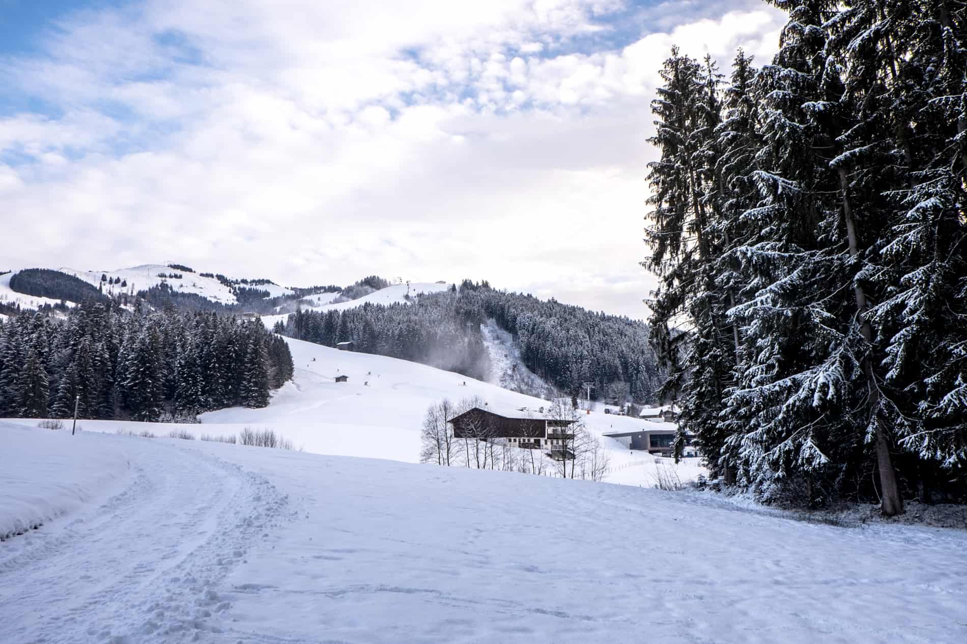 An alpine hill top with a snow covered forest slope and wooden mountain hut. 