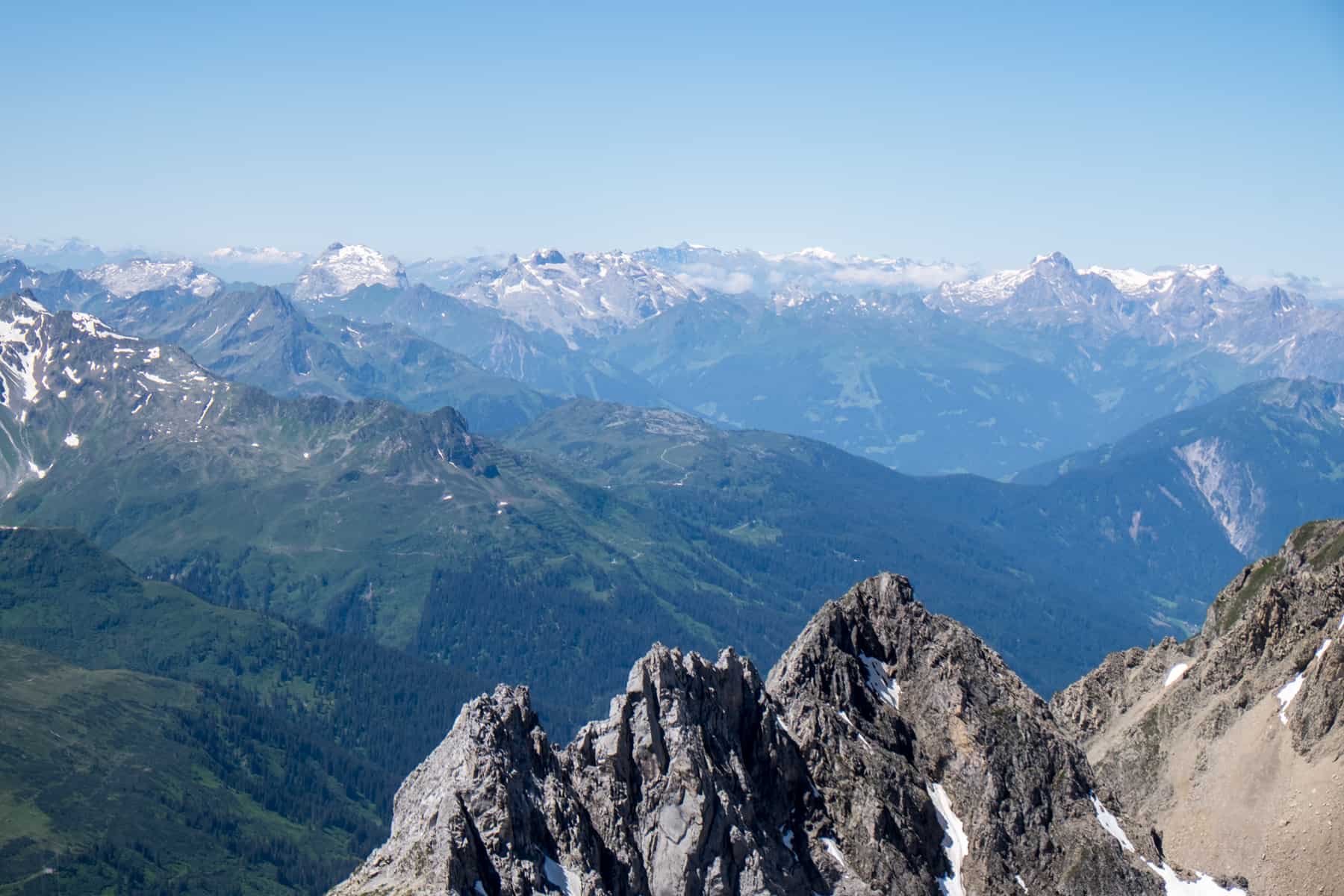 Three jagged rocks in front of a far viewpoint across the Alps of Italy and Switzerland from the Valluga Mountain in St. Anton in Austria