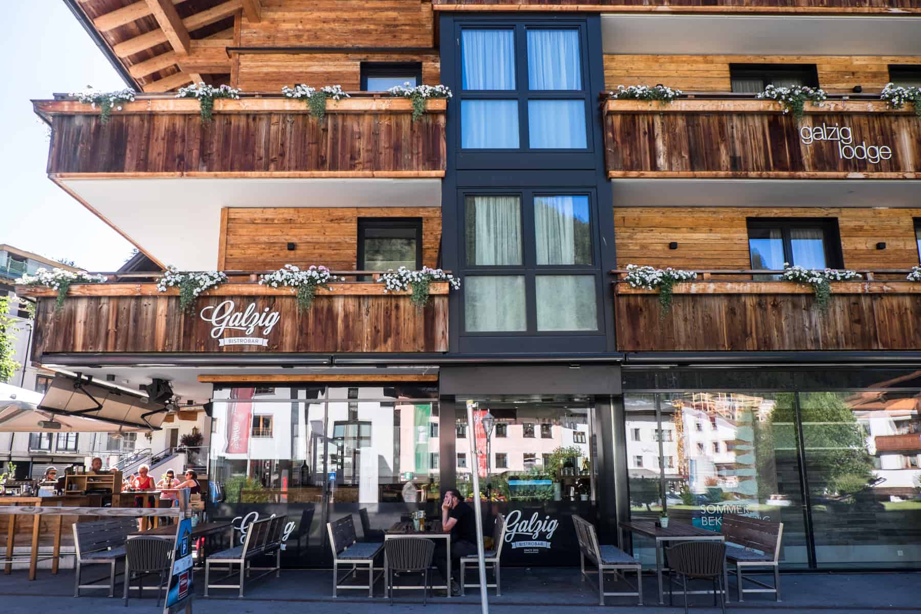 People sitting outside the modern wooden building of the Village Galzig Bar St Anton am Arlberg