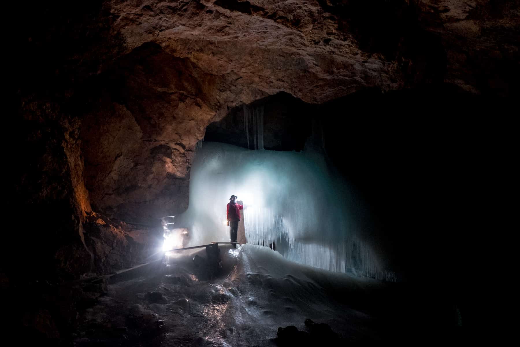 A guide in a red coat stands in front of a boxed shaped sheet of blue illuminated ice in the ice cave Eisriesenwelt in Salzburg, Austria