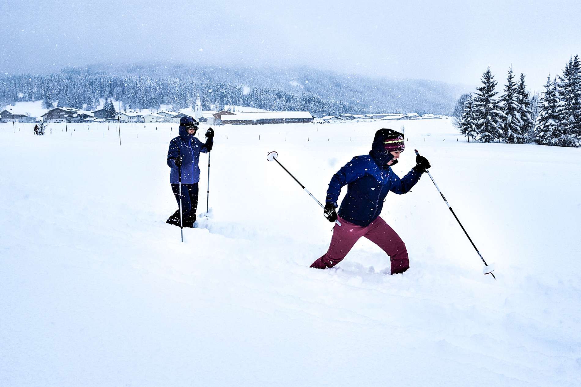 Two women in winter gear hiking knee deep in snow in Austria in winter.