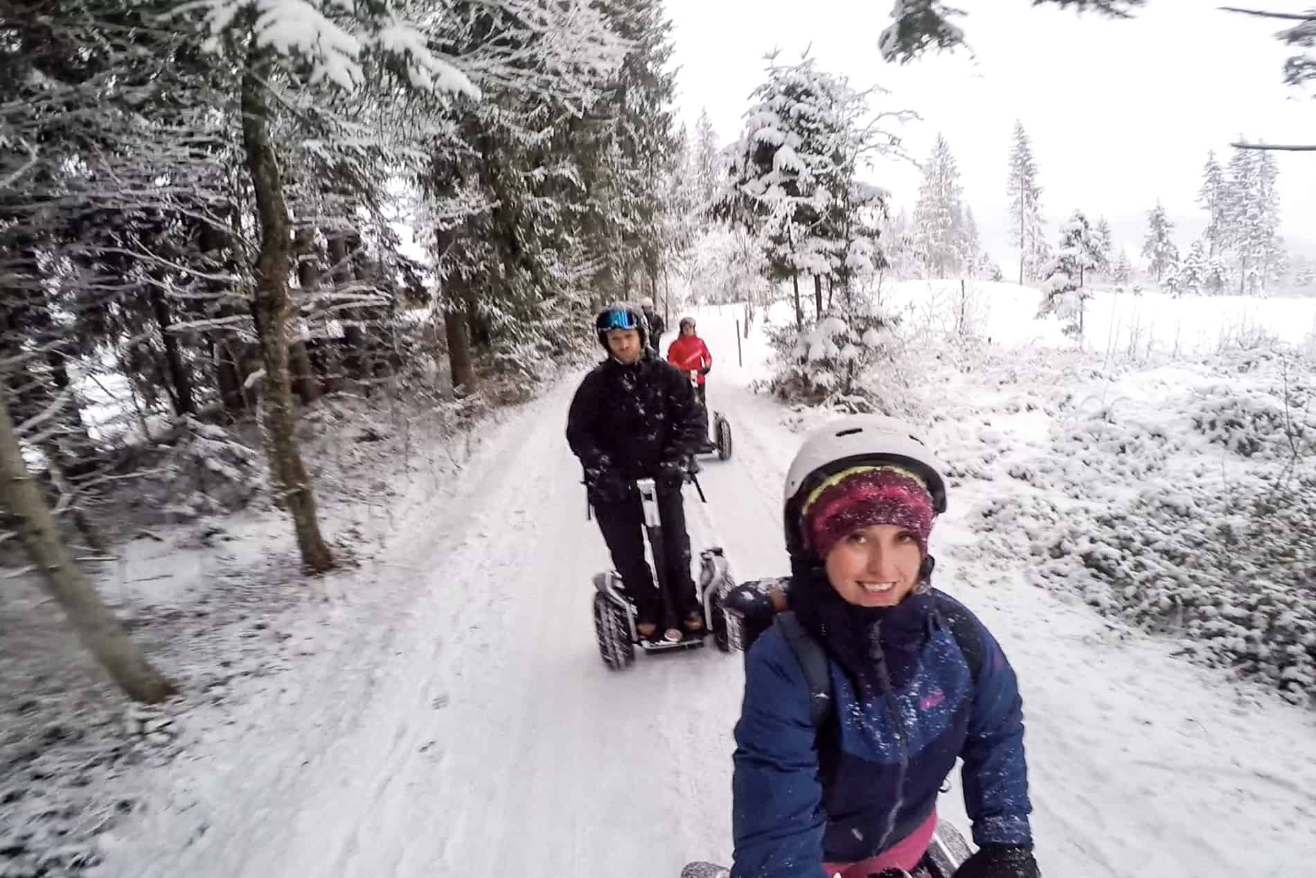 People in winter clothing ride segways in the snow. 