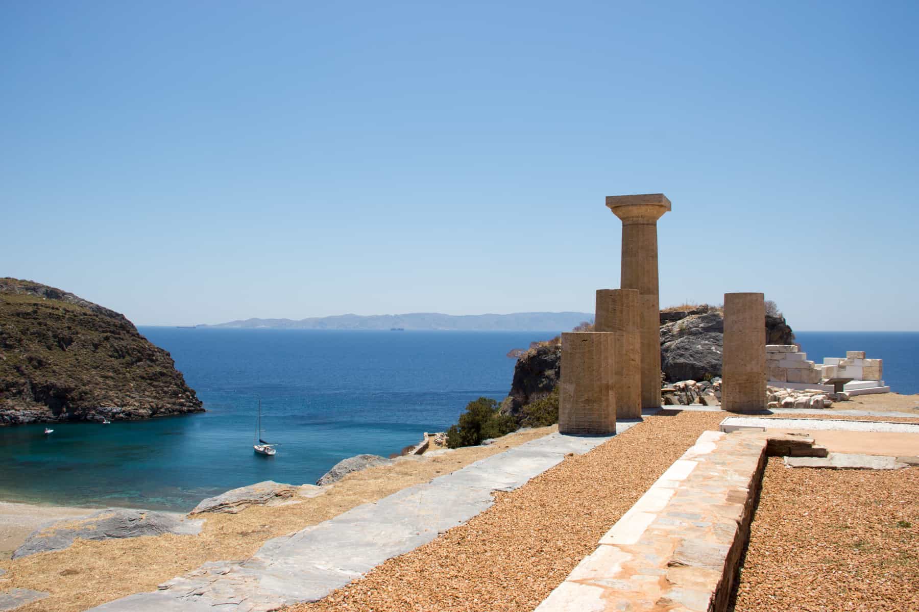 The four columns of the Temple of Athena sit on a hillside of the ancient city of Karthea in Kea island, overlooking the shimmering blue ocean water.