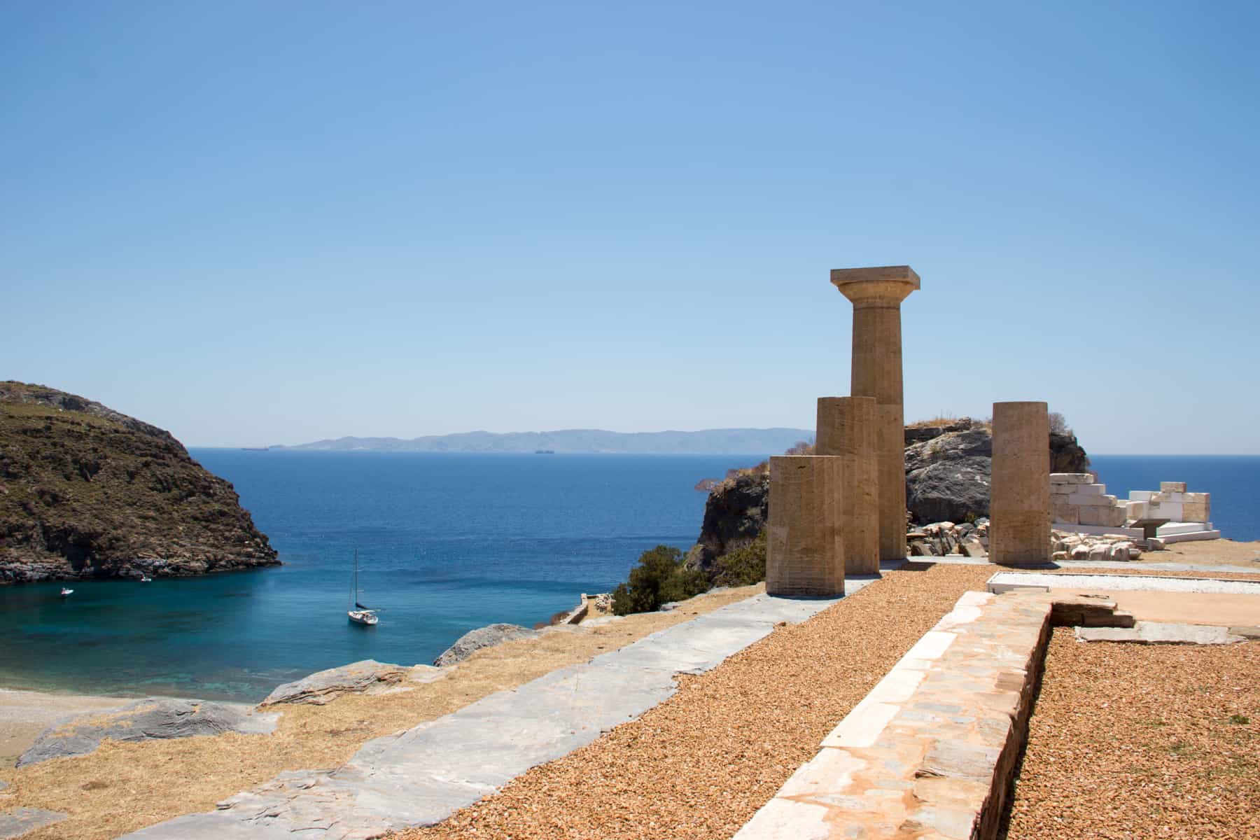 The remains on four ancient greek columns on a square stone foundations overlooking a beach cove and bright blue sea on Kea Island, Greece