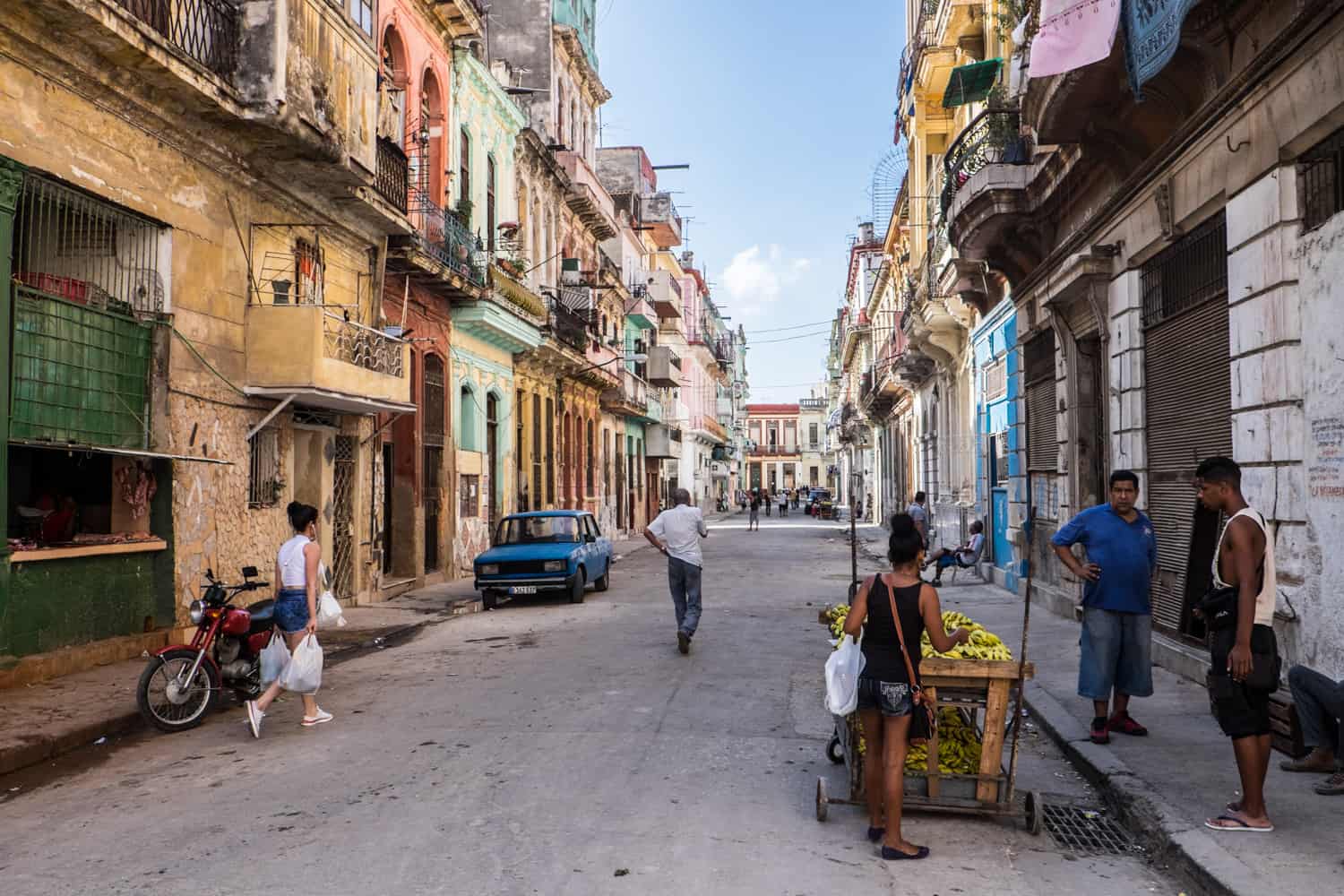 People on a street in Havana, lined with densely packed colourful buildings. 