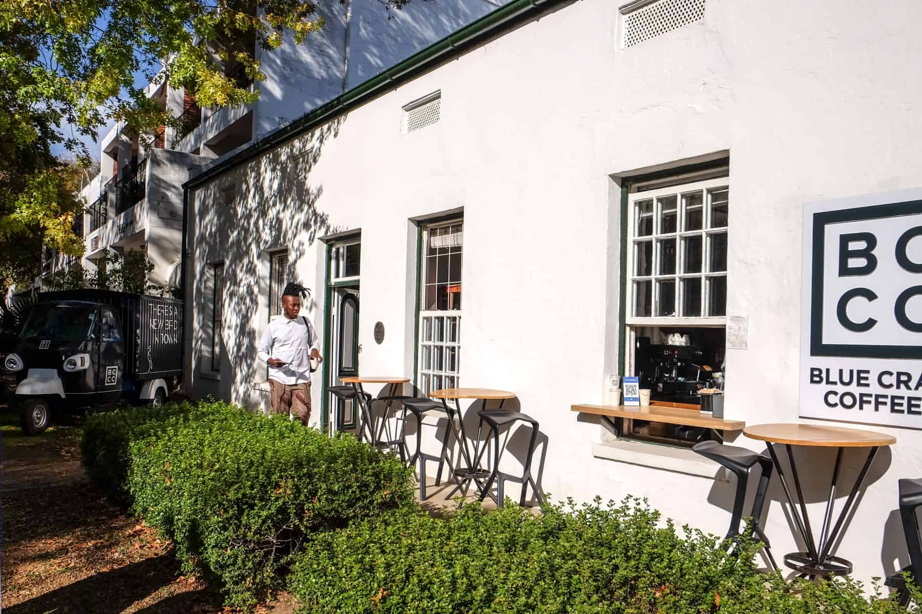 A man walks into a low rise white building with a blue BCCO logo in Stellenbosch set behind a green hedgerow