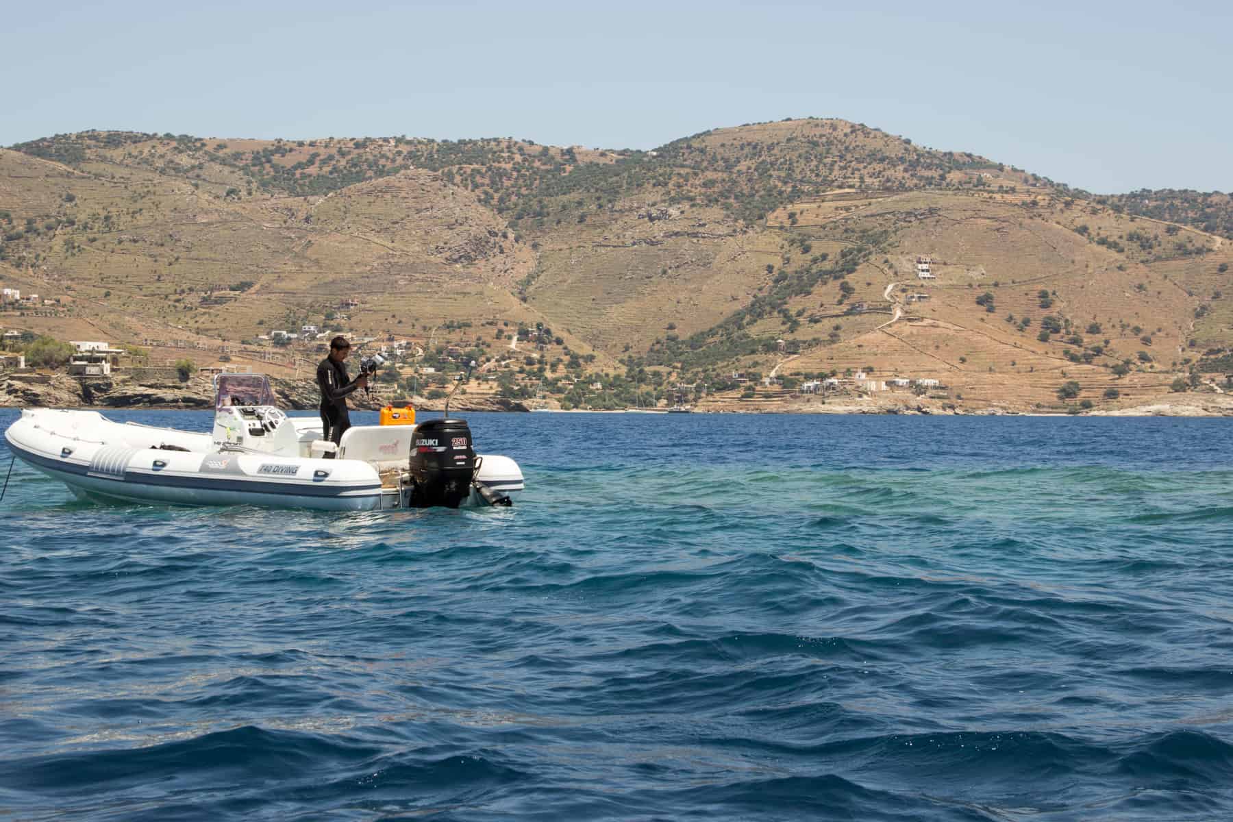 A diver in black scuba gear prepars to jump off a white boat into the seas of Kea Island Greece
