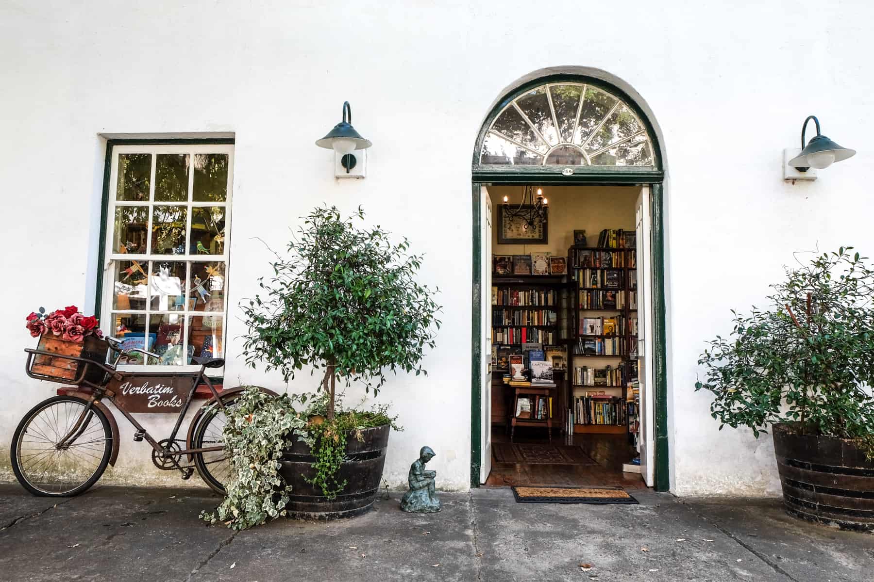 A bike rests against the wall of a white building, and a curved doorway reveals bookcases inside 