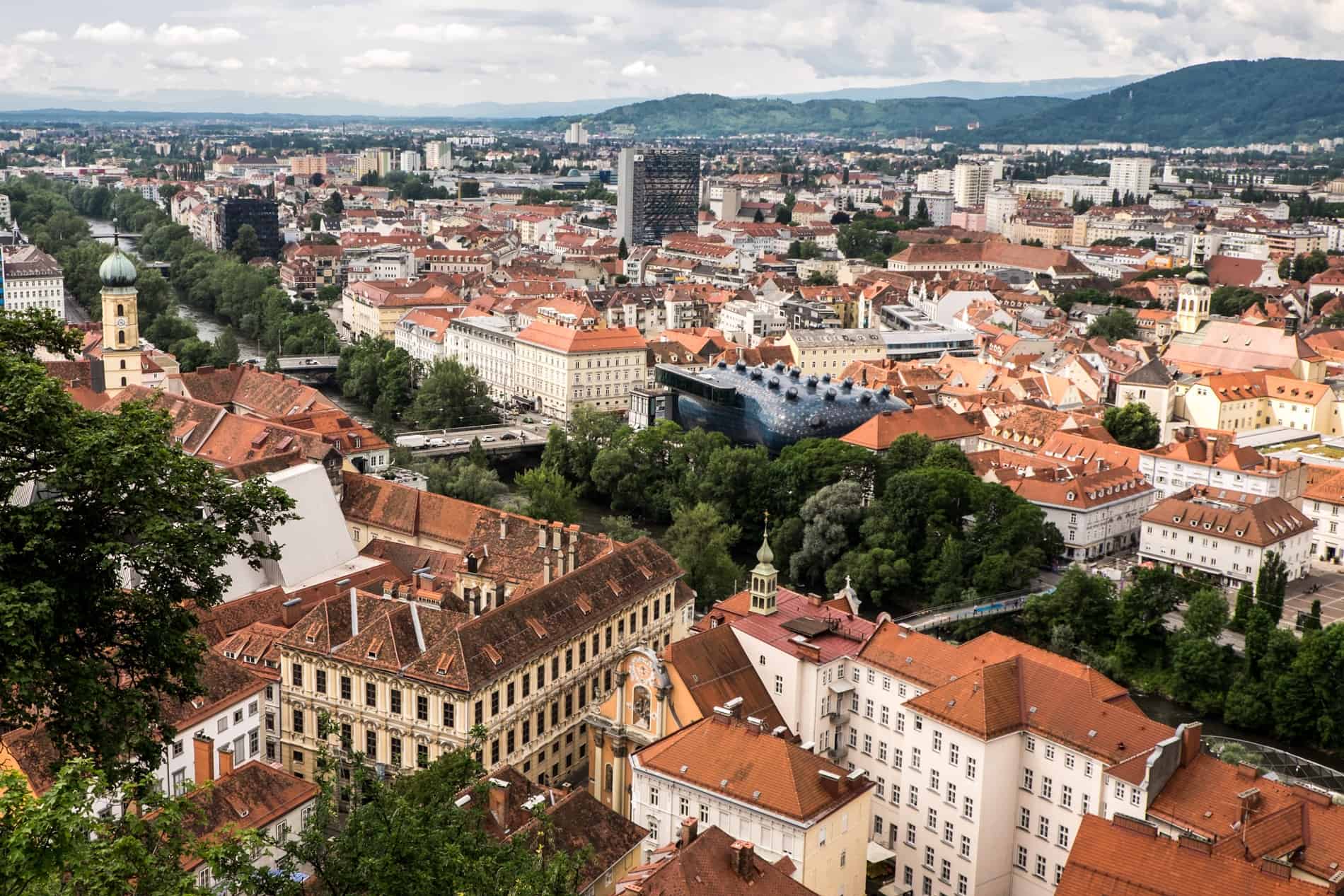 Elevated view of the old and new architecture, red roofed buildings and blue alien-looking art museum of Graz from the Schlossberg hill. 