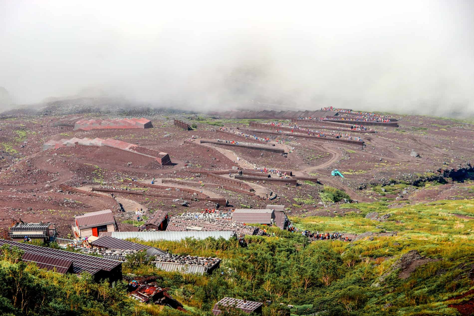 People in colourful hiking clothing climbing Mt. Fuji in Japan on a zigzag of hiking trails through red volcanic soil. 