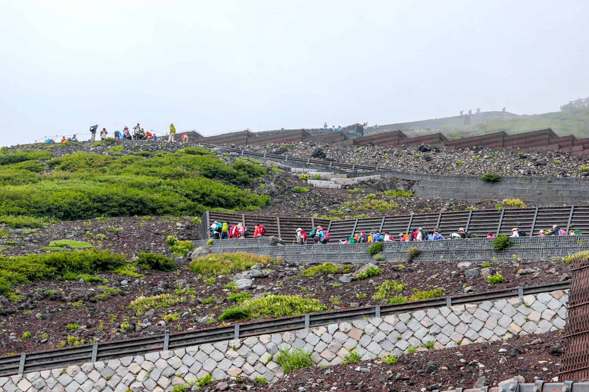 Mountain hikers in multicoloured clothing ascent a zig zag pathway on Mt Fuji, Japan.