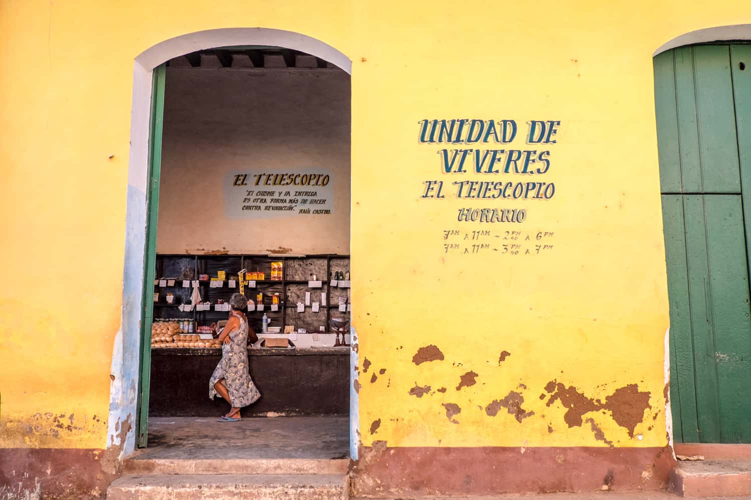 A woman inside a ration store in Cuba, with near empty shelves and a small pile of bread. 