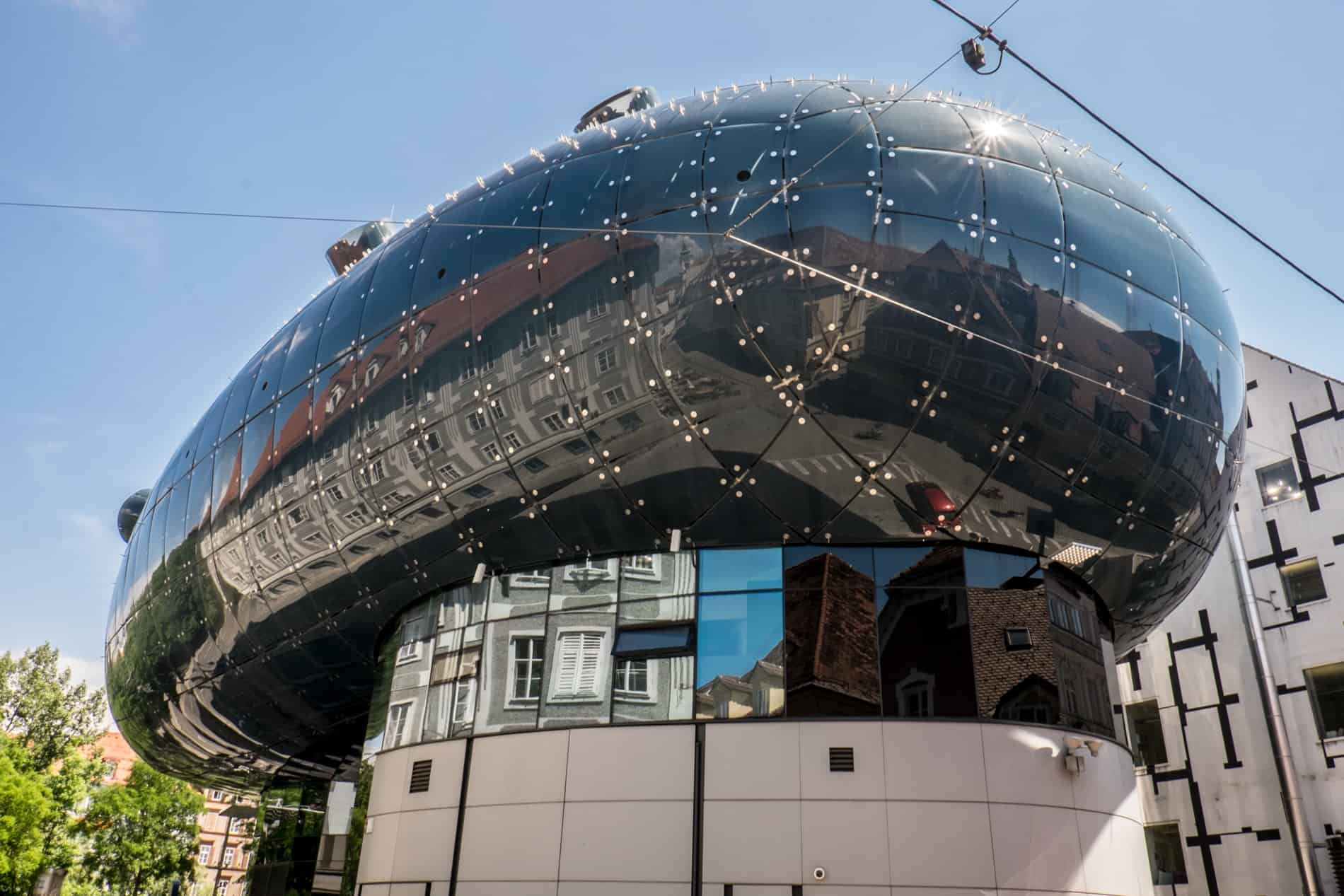 Reflections of old Graz buildings on the modern exterior of the round, blue art museum. 