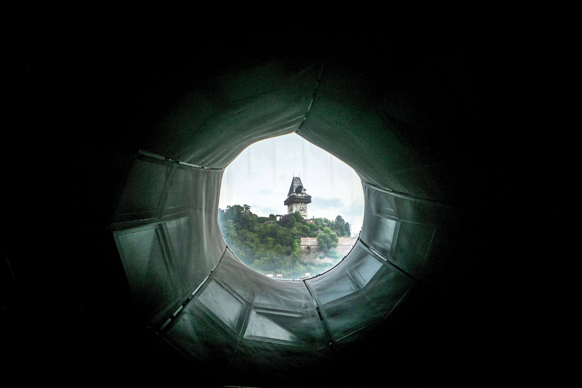View of the Graz clocktower on the hill from a portal window inside the Kunsthaus modern art museum roof.