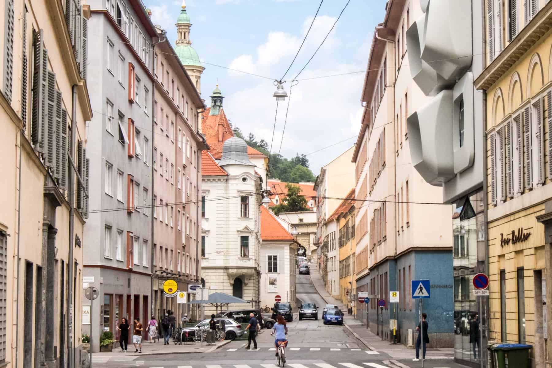 A street field with pastel hued houses and a modern bulbous, bubble design of the ARGOS building by Zara Hadid in Graz, Austria.