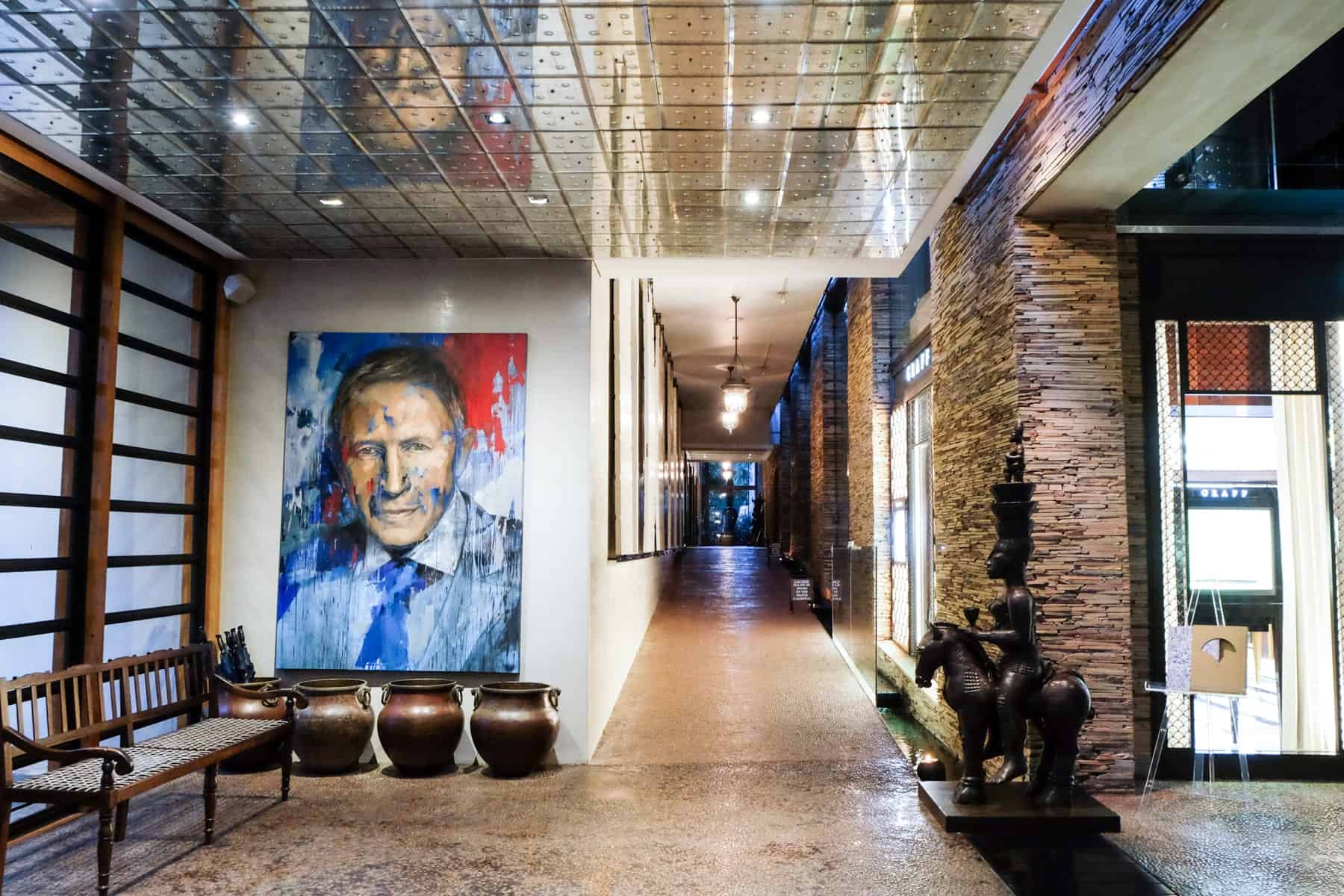 A painting of a man, reflective ceiling and the modern white and exposed wall interior of the artistic Delaire Graff Estate in Stellenbosch 