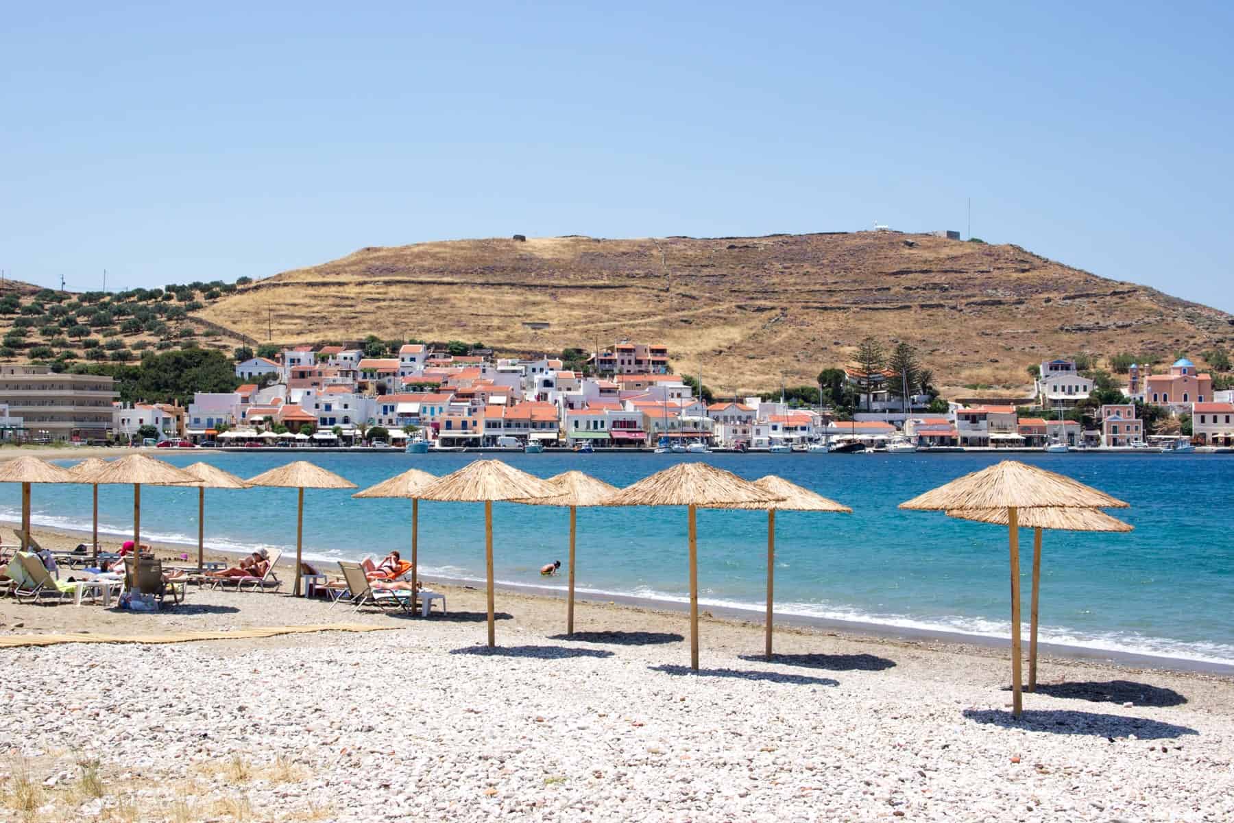 Straw umbrellas in a row on a stoney beach in the coastal town of Korissia on the Greek Kea island
