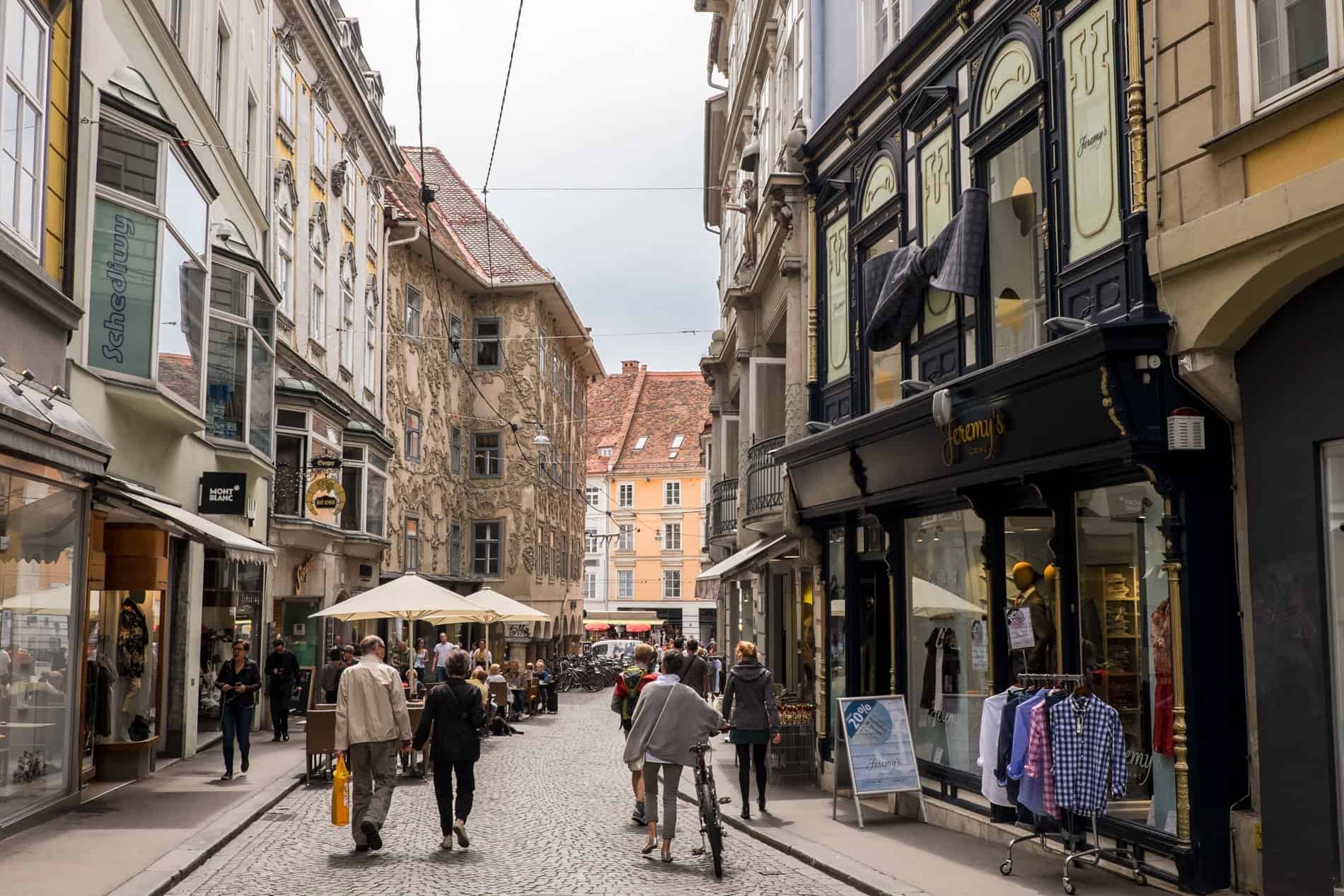 People walking down the beautiful, old Sporgasse street in Graz lined with decorated facades and exquisite shopfronts.
