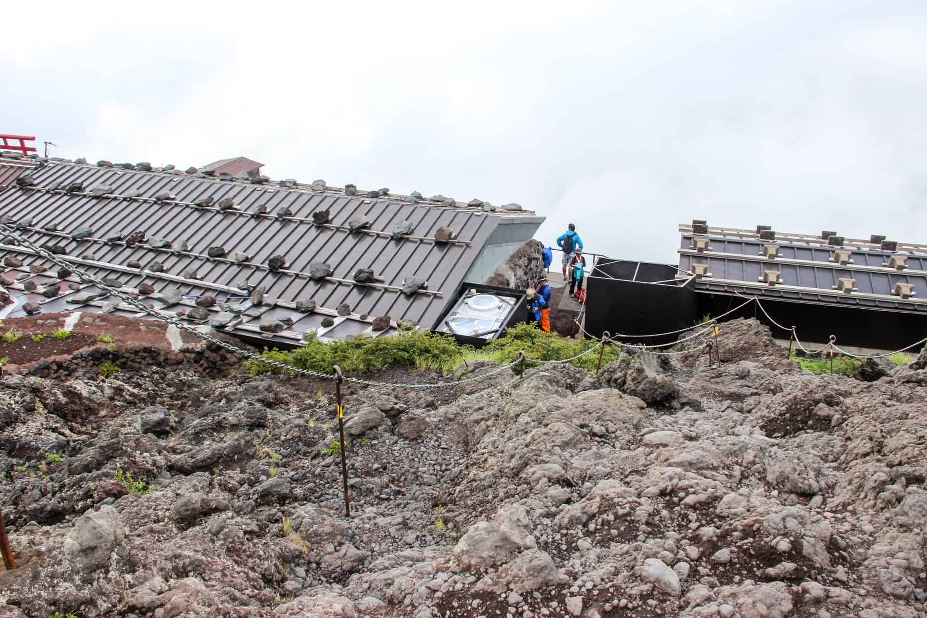 The roofs of mountain huts on Mt. Fuji shruded in fog, with hikers standing in between.