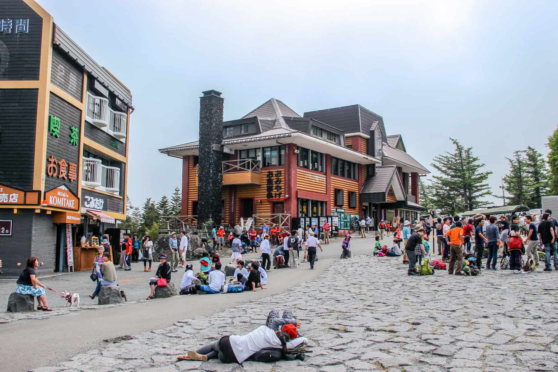 Hikers standing and resting outside two modern buildings at the Mt. Fuji 5th Station. 